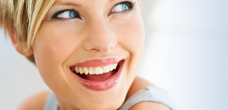 A blond woman with blue eyes smiles and looks over her shoulder.